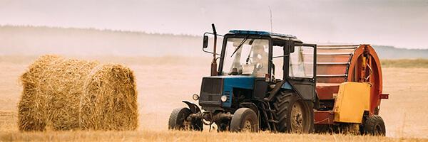 Seguros Agrarios - Tractor azul en el campo recogiendo paja para dar de comer al ganado